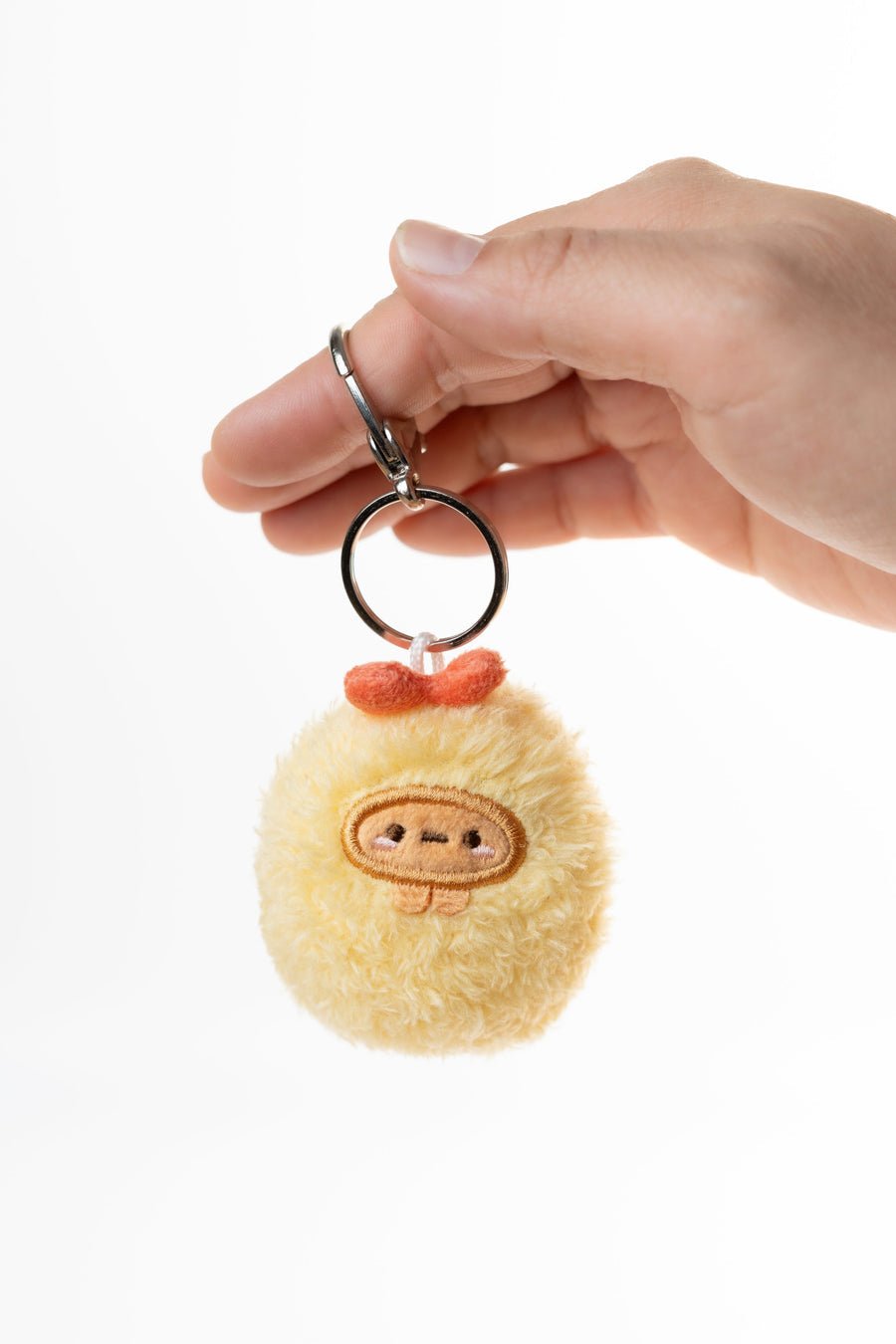Hand holding a fluffy keychain with a cute face design on a white background