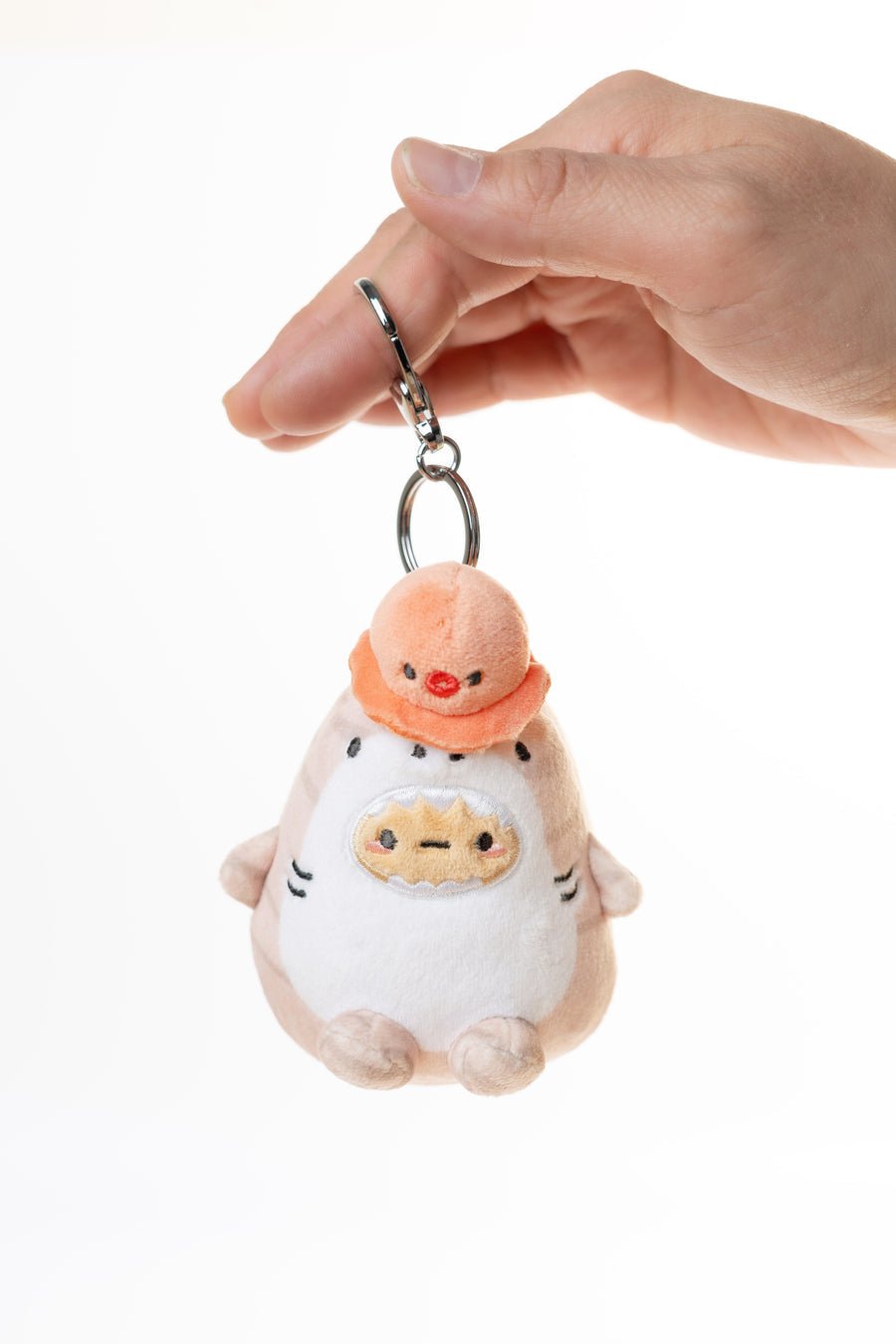 Plush keychain of a cartoon character with a peach-colored hat held by a hand on a white background