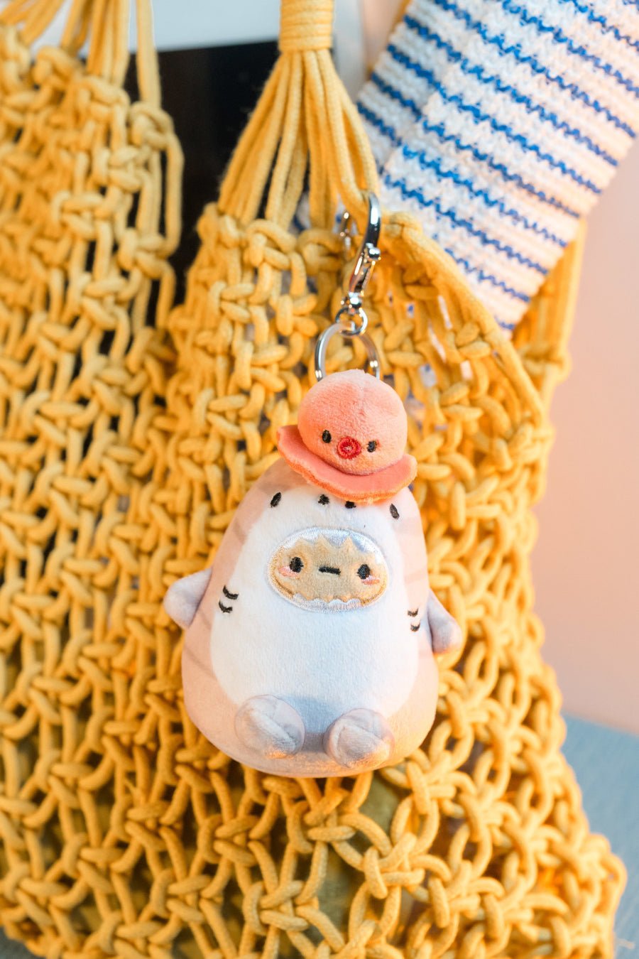 Plush keychain with a peach-colored hat on a yellow textured bag