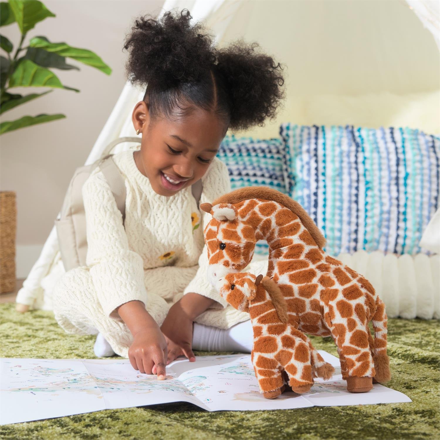 Child reading a book with a plush giraffe toy on a green carpet