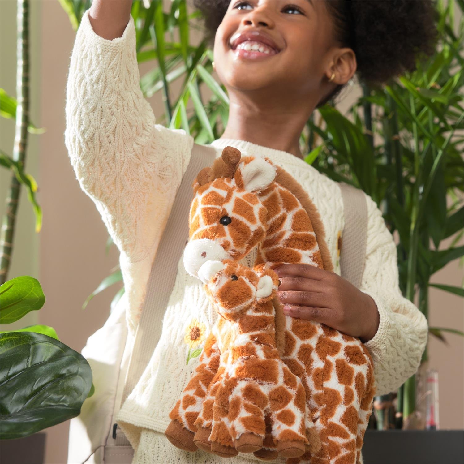 Child holding a plush giraffe toy with plants in the background