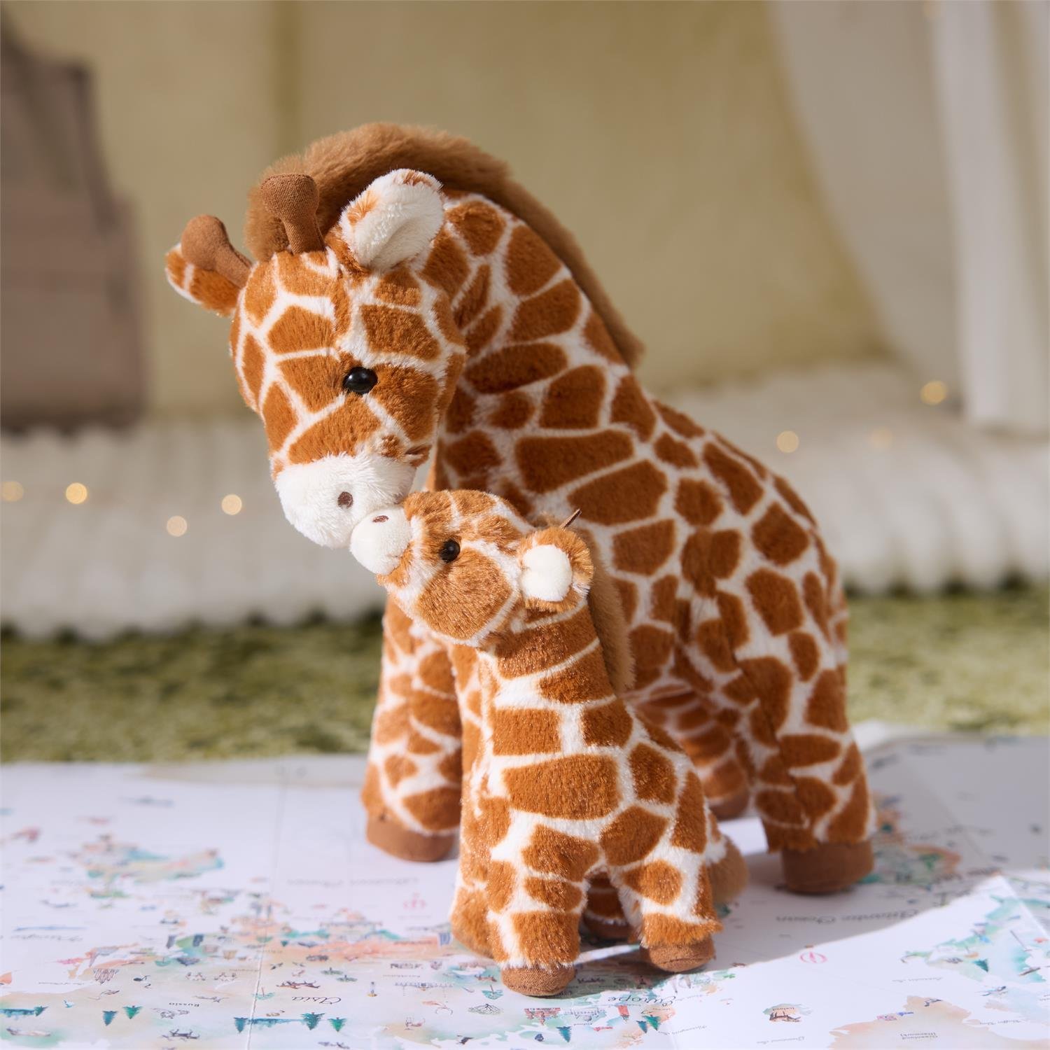Two plush giraffes, one larger and one smaller, on a patterned surface with a blurred background.
