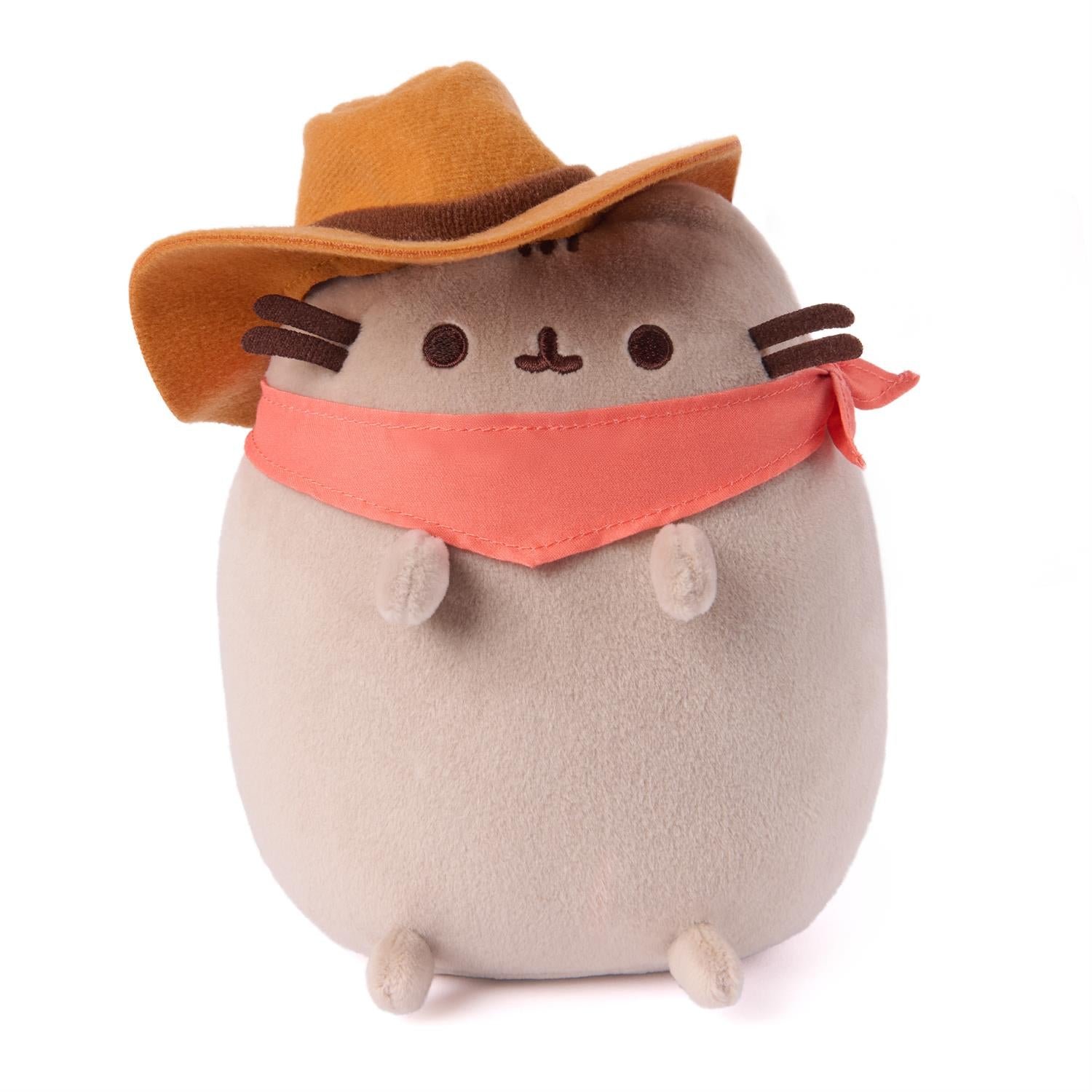 Plush toy resembling a cat in a cowboy outfit with a brown hat and bandana on a white background