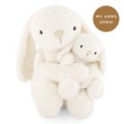 Two cream-colored plush bunnies embracing each other on a white background with a brown circle and text.