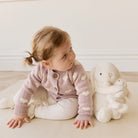 Child in a polka dot cardigan sitting on a light-colored floor with a white teddy bear.