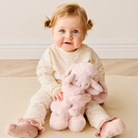 Soft pink plush hugging bunny set by Snuggle Bunnies, mama and baby bunnies nestled together, held by a smiling baby in floral onesie, lifestyle front view